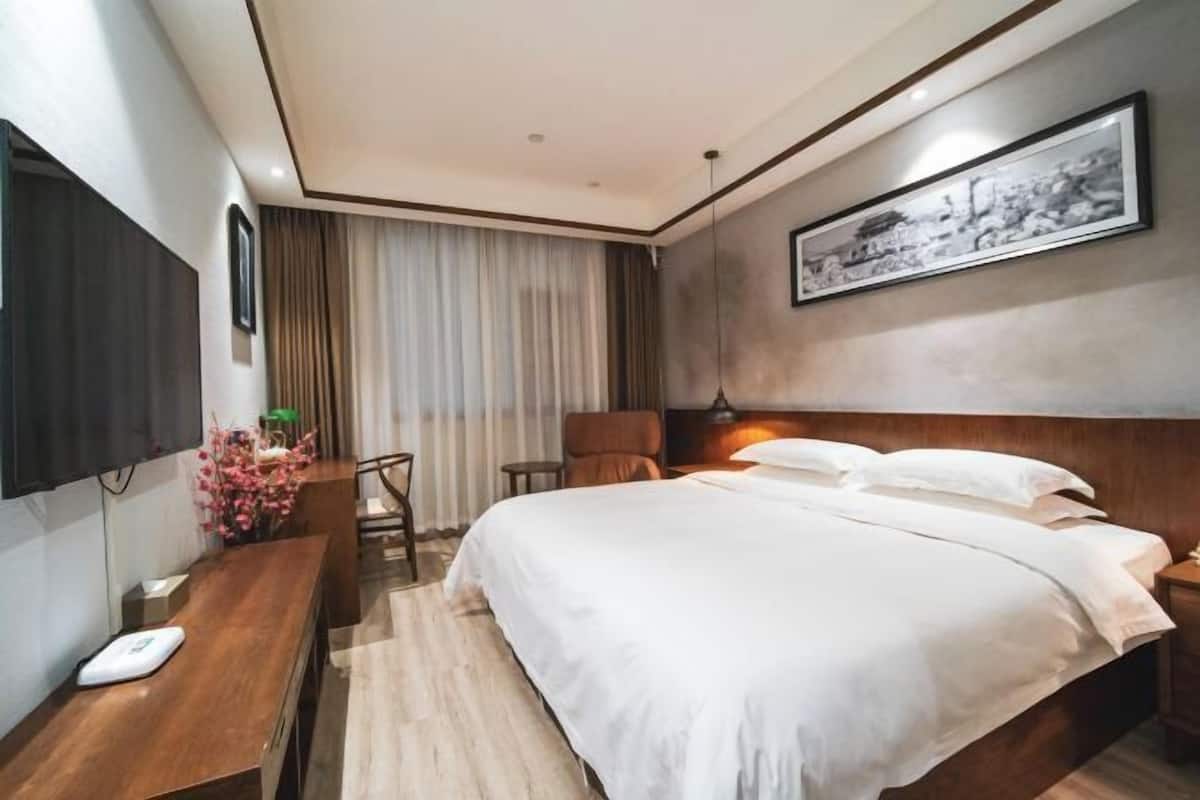 Una habitación de hotel con cama, escritorio, silla, televisión y un cuadro en la pared.