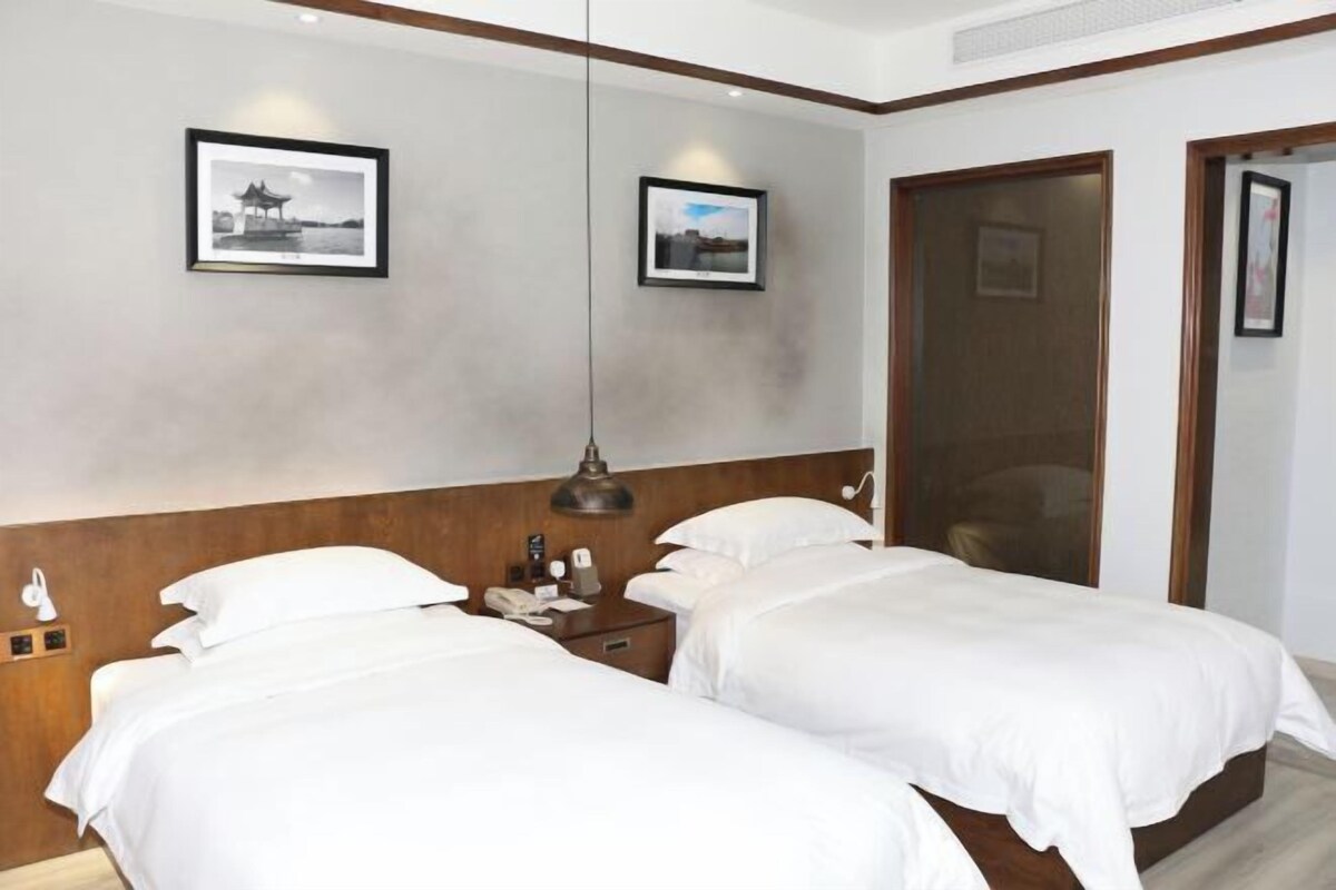 Una habitación de hotel con dos camas, un cabecero de madera, una mesita de noche con lámpara y dos cuadros en la pared.