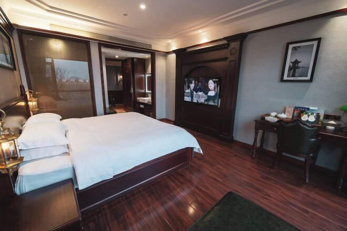 Habitación de hotel con una cama grande, un escritorio, una silla, un televisor y un cuadro en la pared.