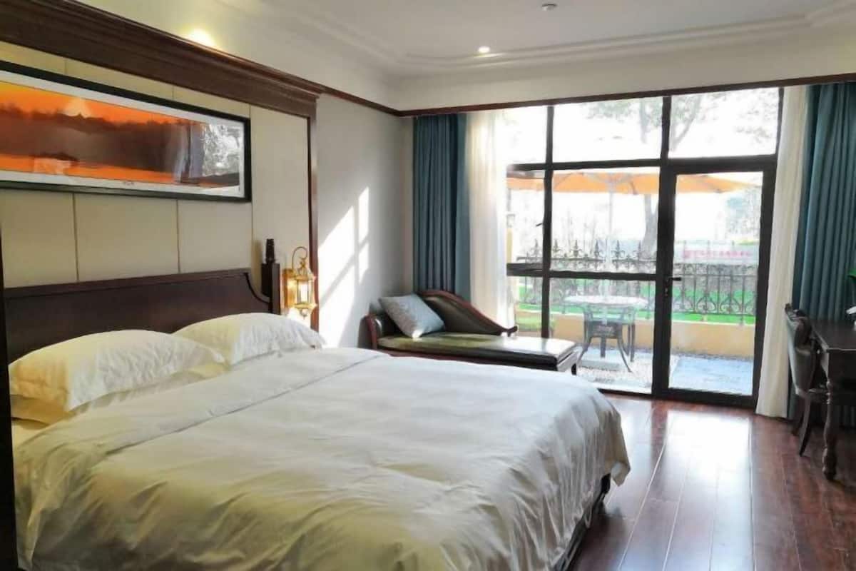 Una habitación de hotel con una cama grande, un área de estar con vistas y un balcón con mobiliario exterior.