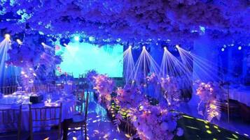 An indoor venue with tables and chairs arranged for an event, decorated with floral arrangements and draped fabric.