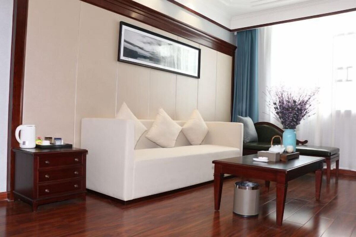 Ein Hotelzimmer mit Sofa, einem kleinen Tisch, einem Nachttisch, einer Mülltonne, einer Blumenvase und einem gerahmten Bild an der Wand.