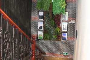 Eine Treppe mit aufwendiger Metallreling und einer Backsteinmauer, versehen mit gerahmten Bildern und einem vertikalen Garten.