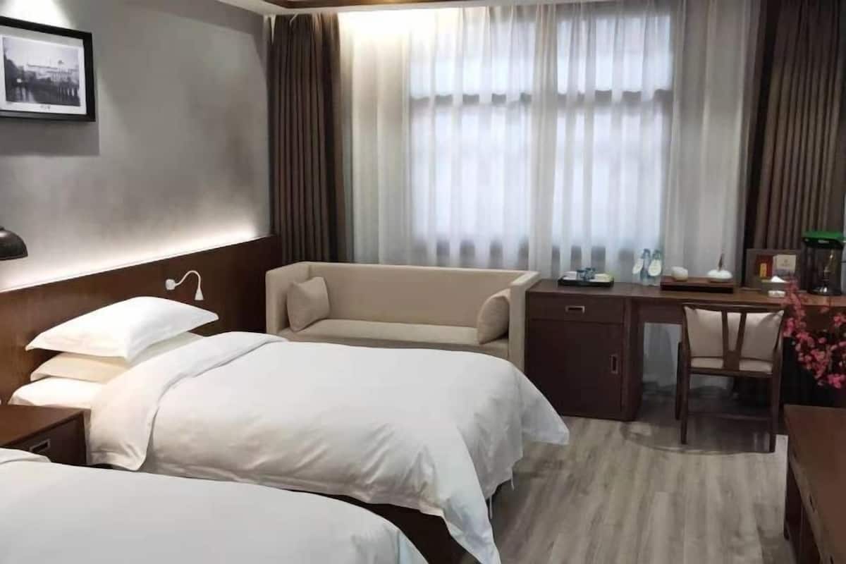Habitación de hotel con dos camas, un escritorio, una silla y un ventanal con cortinas.