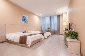 Quarto de hotel com duas camas, uma mesa com luminária, um espelho e uma planta.