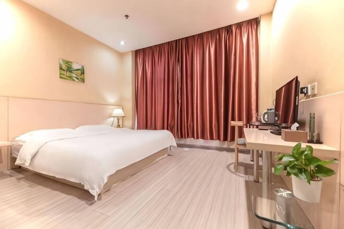 Una habitación de hotel con cama, mesita de noche, lámpara y una planta en maceta.