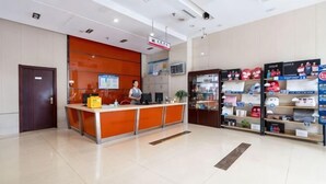 A reception area with a counter, a man standing behind it, and a display of various items on shelves to the right. - Binle Business Express Hotel (Shijiazhuang)