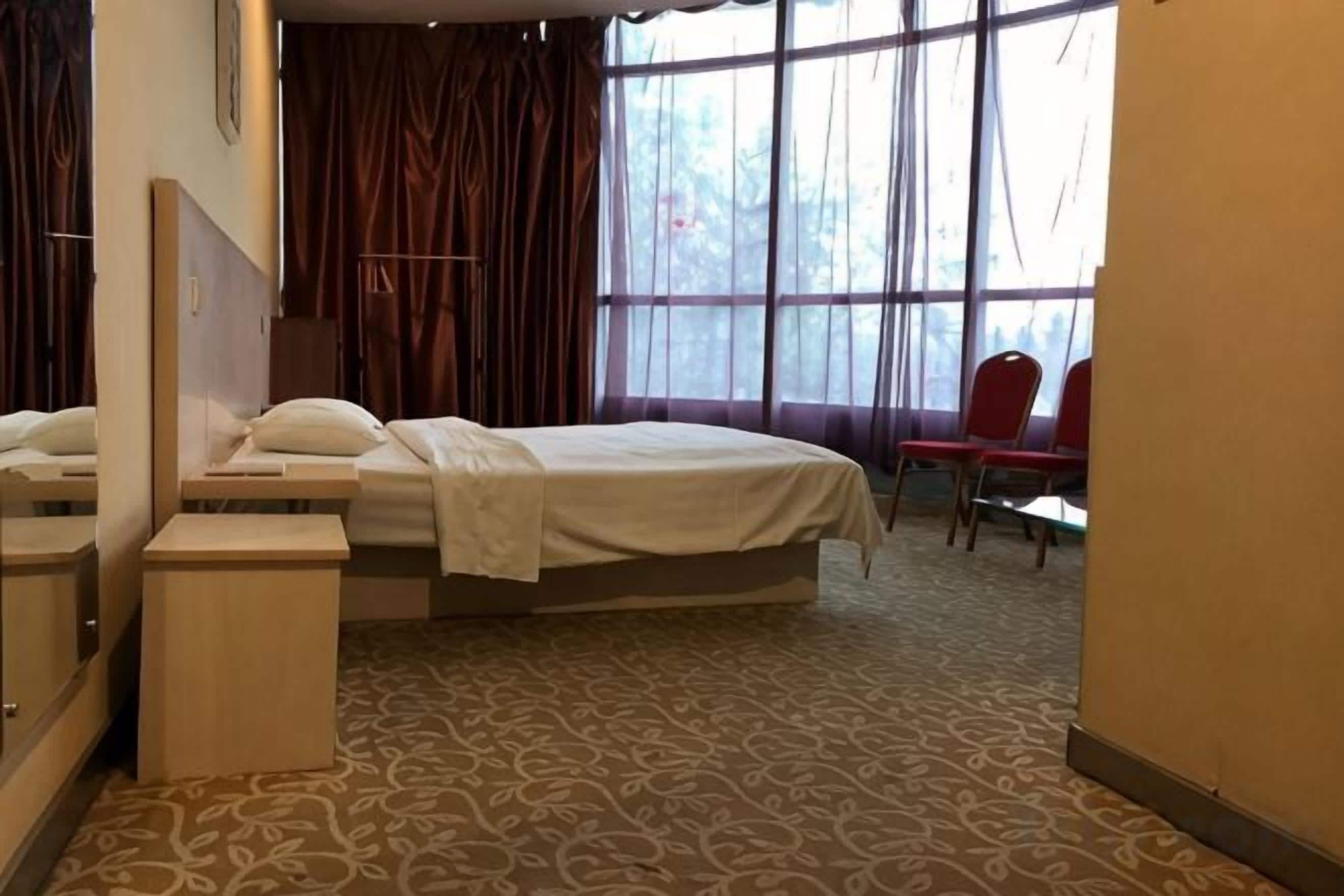 A hotel room with a bed, a small table, a mirror, and a window with curtains.