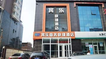 A hotel with a prominent sign, a glass facade, and a parking area with cars.