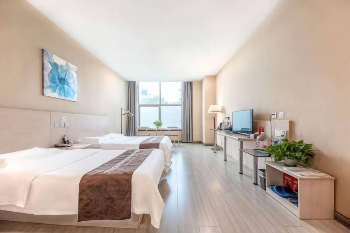 Habitación de hotel con dos camas, un escritorio con computadora, televisor y ventana con cortinas.