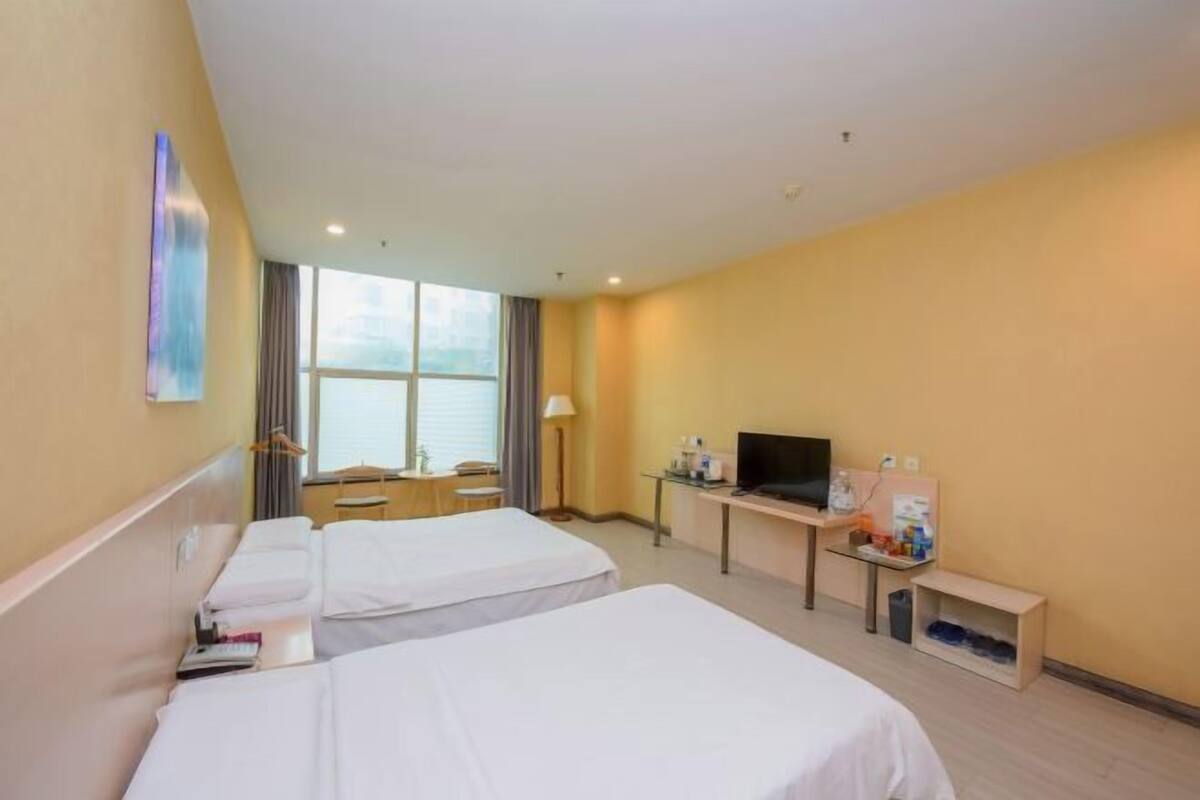 Habitación de hotel con dos camas, un escritorio con televisor, una ventana y vista al mar.