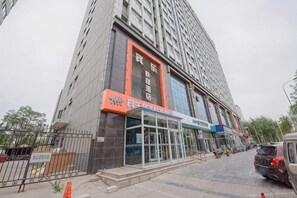 A multi-story building with a glass entrance, a sign with Chinese characters, and a parked car. - Binle Business Express Hotel (Shijiazhuang)