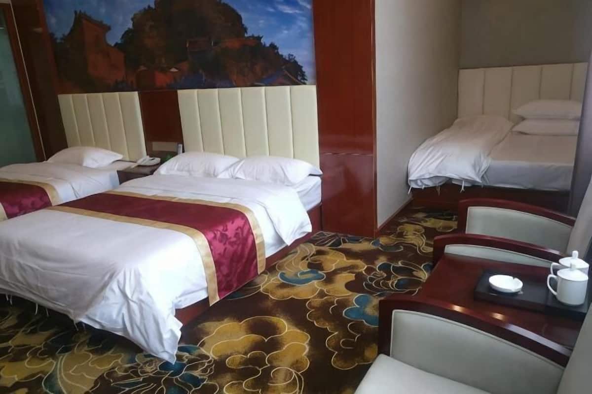 A hotel room with two beds, a dining table with a teapot, and a mural on the wall.