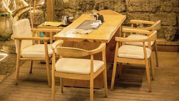 A wooden dining table with four chairs, set on a wooden deck with a stone wall in the background.