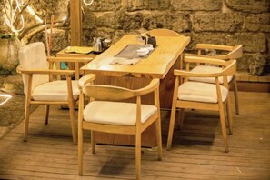 A wooden dining table with four chairs, set on a wooden deck with a stone wall in the background. - Weizhou Island Summer Sunshine Sea View Hotel (Weizhou Island)