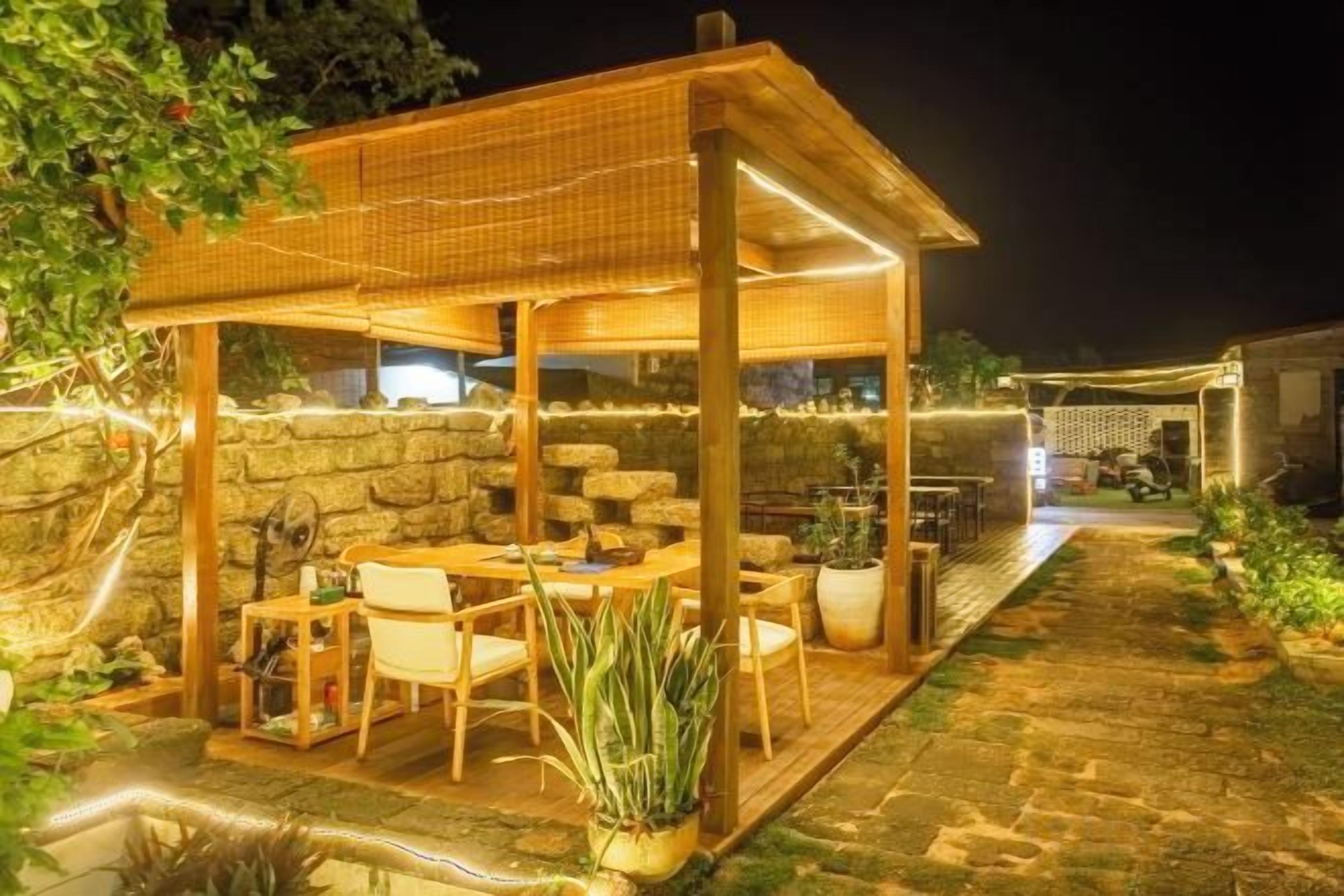 A covered outdoor seating area with tables and chairs, surrounded by stone walls and potted plants.