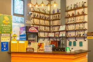 Uma área de bar com prateleiras de garrafas, balcão com cardápios e luminárias penduradas.