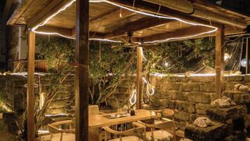 An outdoor wooden pergola with string lights, a table, and chairs.