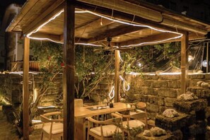 Eine hölzerne Pergola im Freien mit Lichterketten, einem Tisch und Stühlen.