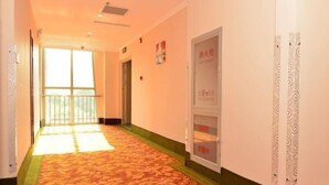 A hotel corridor with a patterned carpet, a large window at the end, and a door with a sign. - Greentree INN Beijing Chaoyang District Second FOR (Beijing)