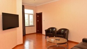 A living room with a flat-screen TV mounted on the wall, two leather armchairs, a round coffee table, and a sofa. - Greentree INN Beijing Chaoyang District Second FOR (Beijing)