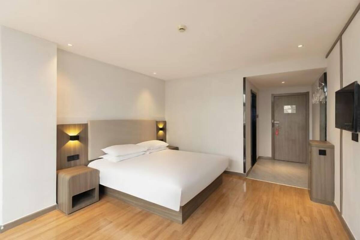 A modern hotel room with a bed, bedside tables, a TV, and a door leading to another room.