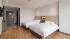 A hotel room with two beds, a wooden floor, a wall-mounted TV, and a door leading to a hallway.