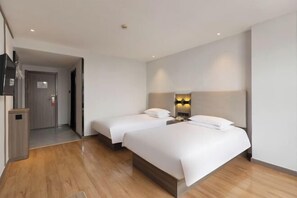 A hotel room with two beds, a wooden floor, a wall-mounted TV, and a door leading to a hallway.