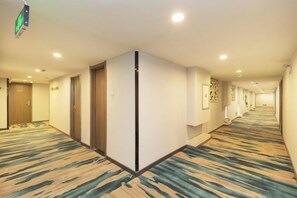 Un pasillo de hotel con suelo alfombrado, puertas y luces empotradas.
