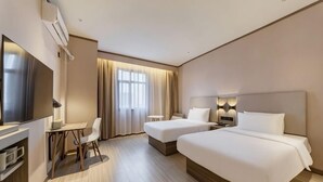 Habitación de hotel con dos camas, un escritorio con silla, televisión y ventana con cortinas.