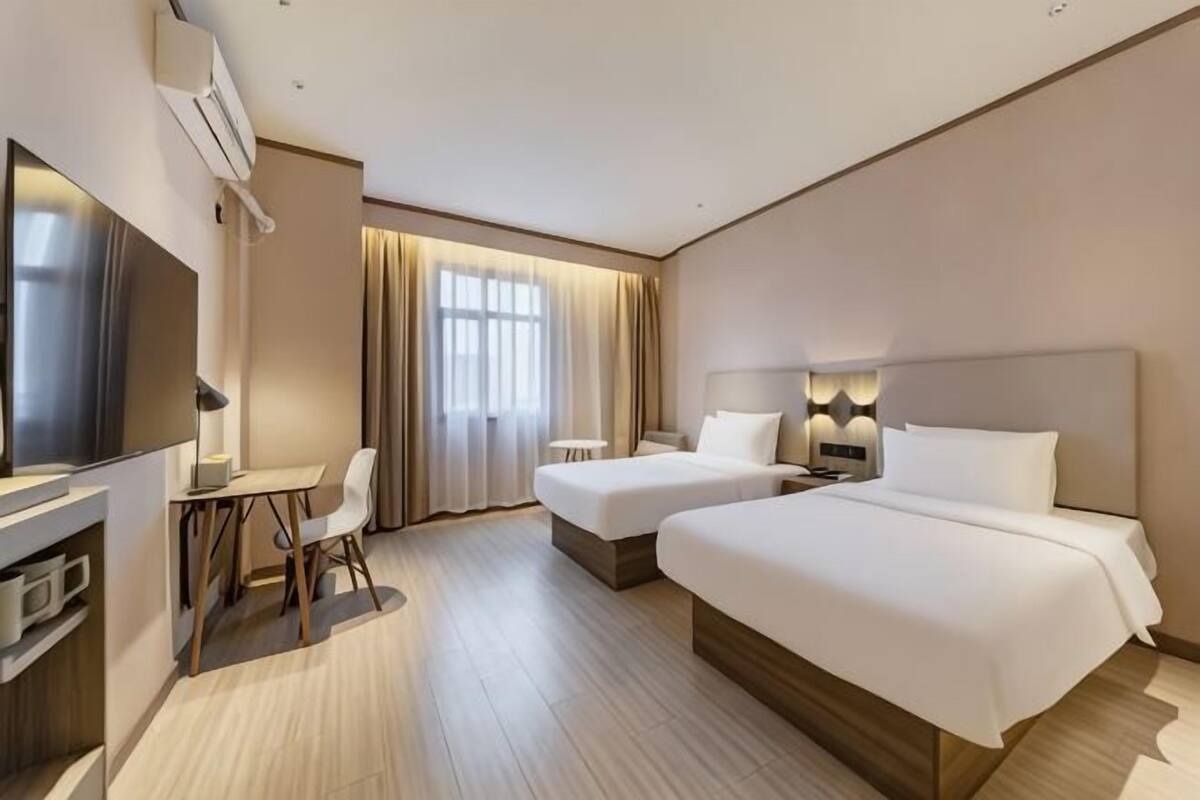 A hotel room with two beds, a desk with a chair, a television, and a window with curtains.