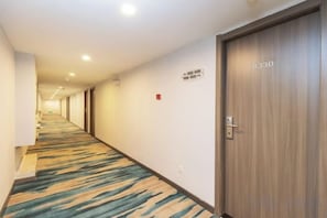 A hotel corridor with carpeted flooring, a wooden door with a number, and a fire alarm on the wall. - Shell Hotel (Xuzhou Xinyi Nanjing Road Railway Station) (XINYI)