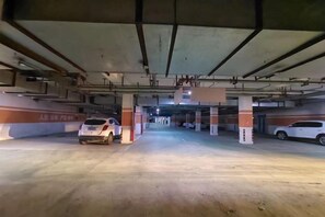An underground parking garage with concrete pillars, a white car parked in the foreground, and another car in the background. - Shell Hotel (Xuzhou Xinyi Nanjing Road Railway Station) (XINYI)