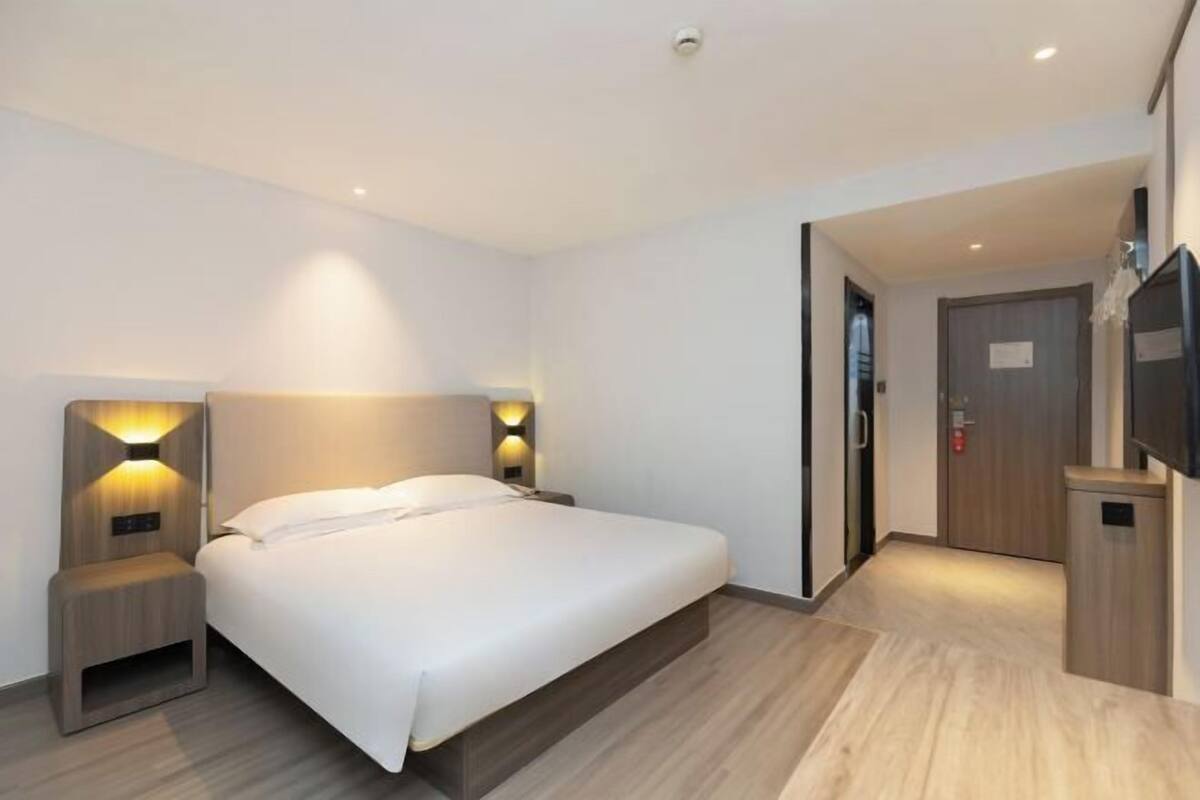 A modern hotel room with a large bed, bedside lamps, a flat-screen TV, and a wooden floor.