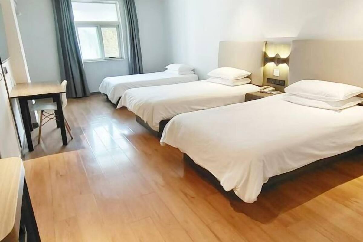 A hotel room with two beds, a desk, and a window with curtains.