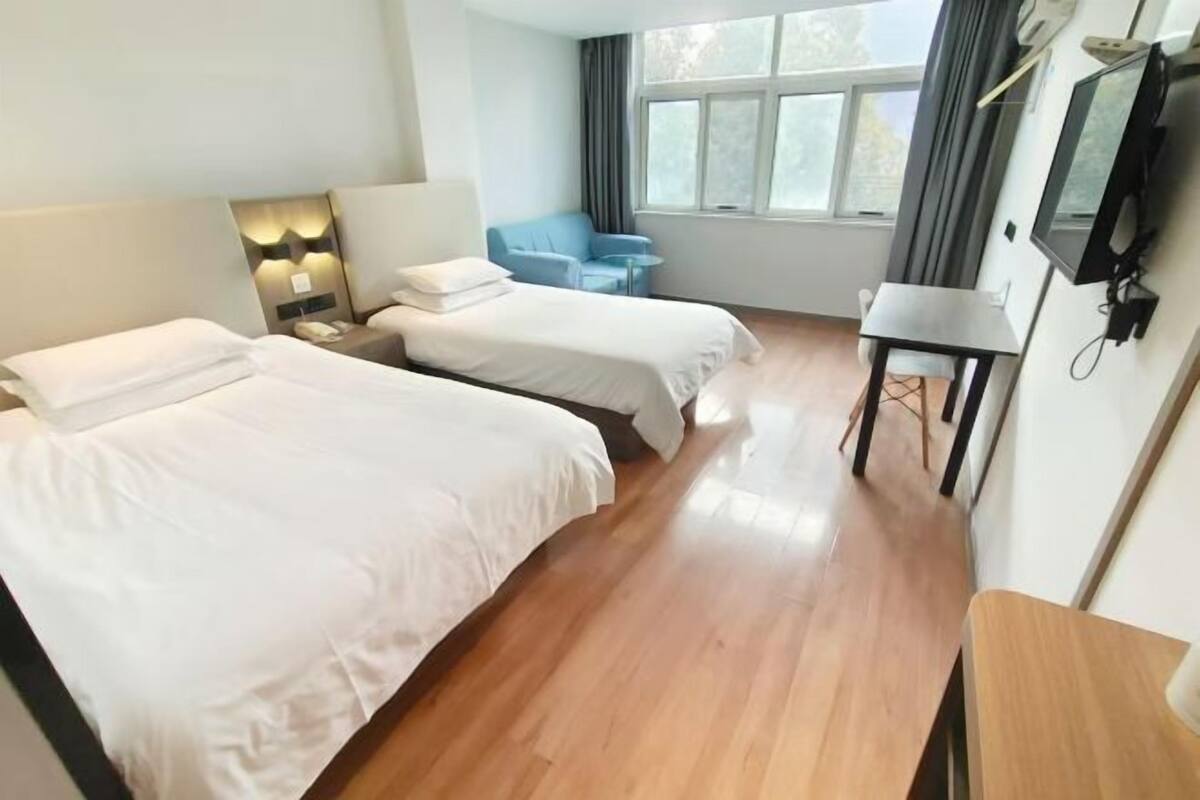 A hotel room with two beds, a small table, a chair, a TV, and a window with curtains.