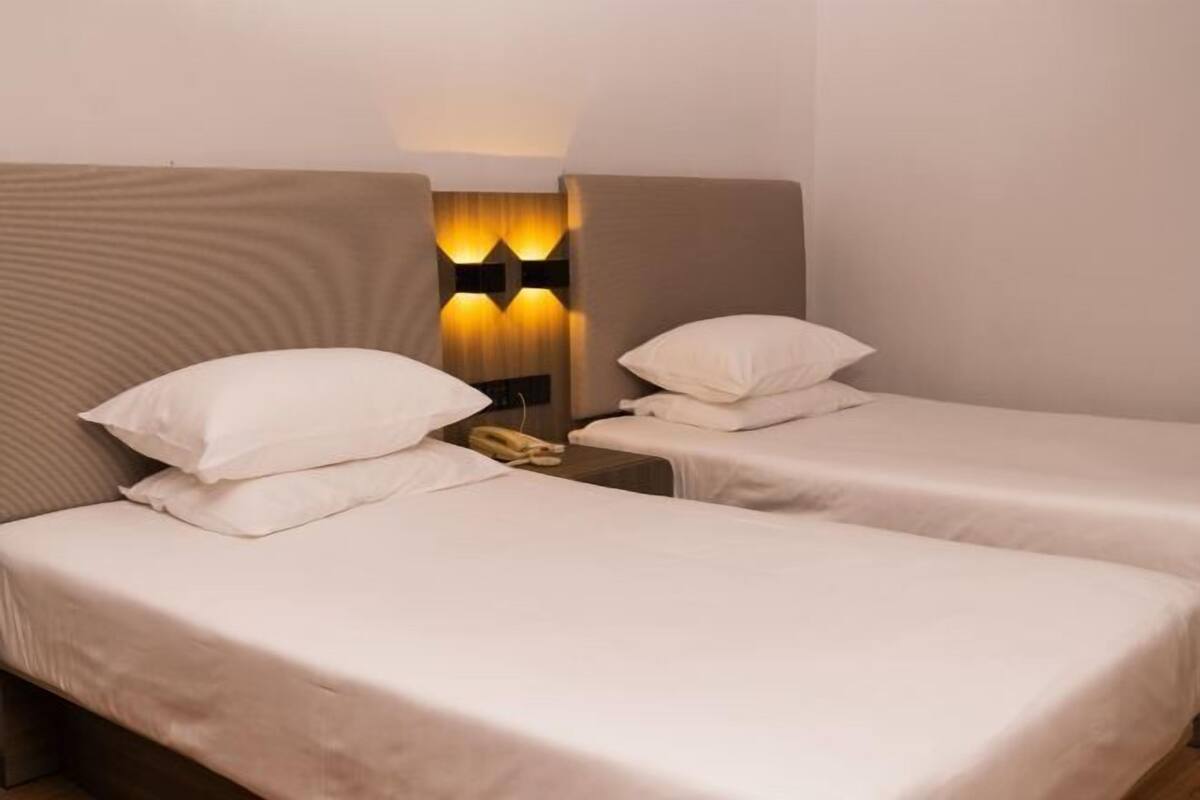 A hotel room with two single beds, a nightstand with a telephone, and a wall-mounted light fixture.