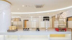 Una moderna zona de recepción de hotel con un mostrador blanco, un separador de vidrio y una máquina de café.