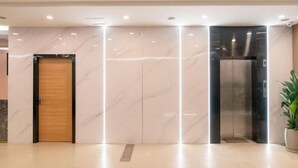 Un ascensor moderno con acabado metálico, junto a una puerta de madera y una pared de mármol.