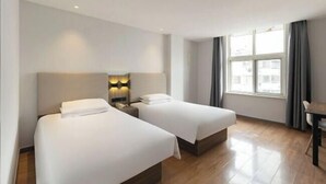 A hotel room with two beds, a desk, a window with curtains, and a city view.