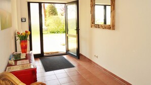 A hotel reception area with a wooden chair, a red table with a vase of flowers, a mirror on the wall, and a door leading outside. - Uns Wiek-Hus (Mönchgut-Granitz)