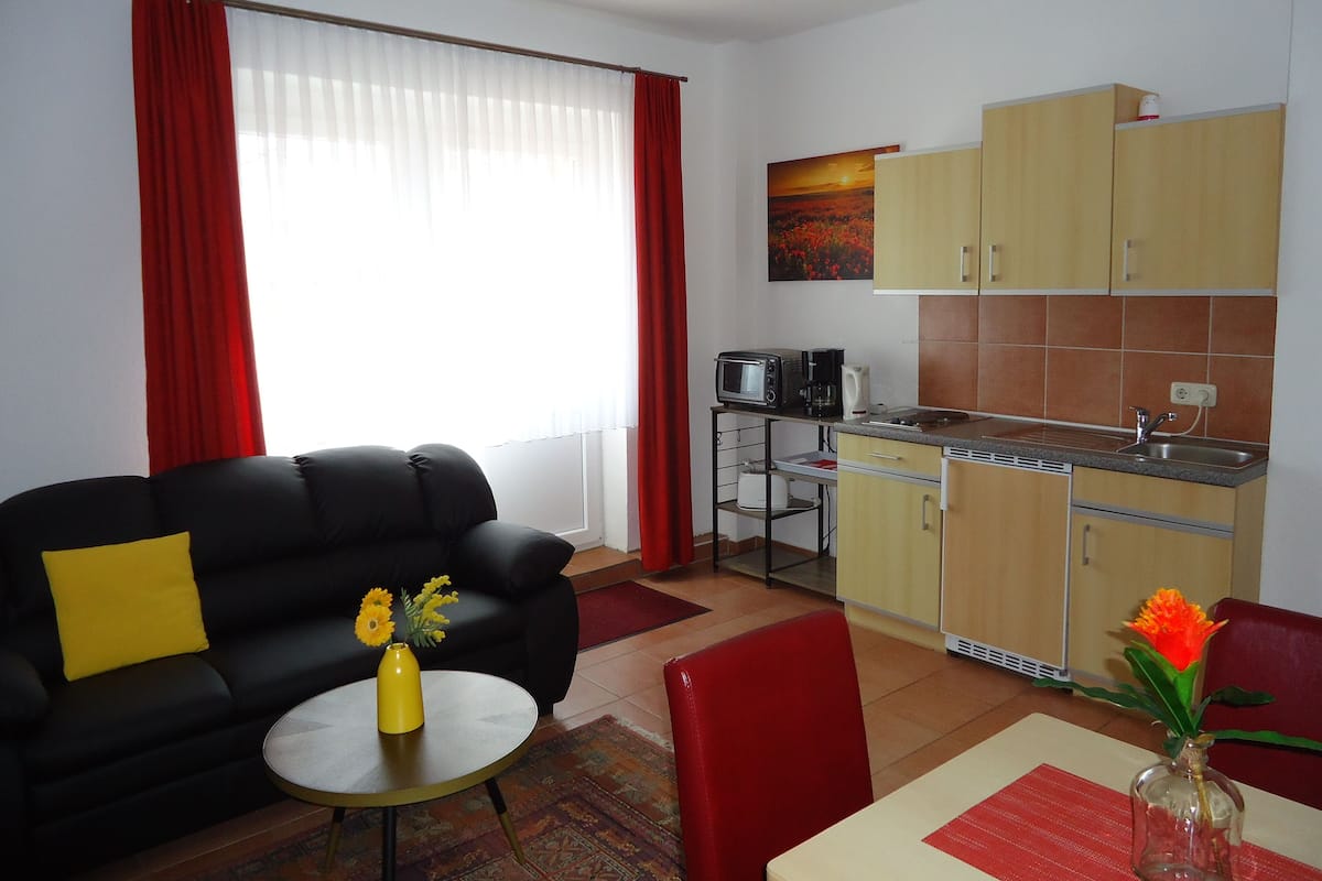 A compact living space with a sofa, a dining table, a kitchen area, and a window with curtains.