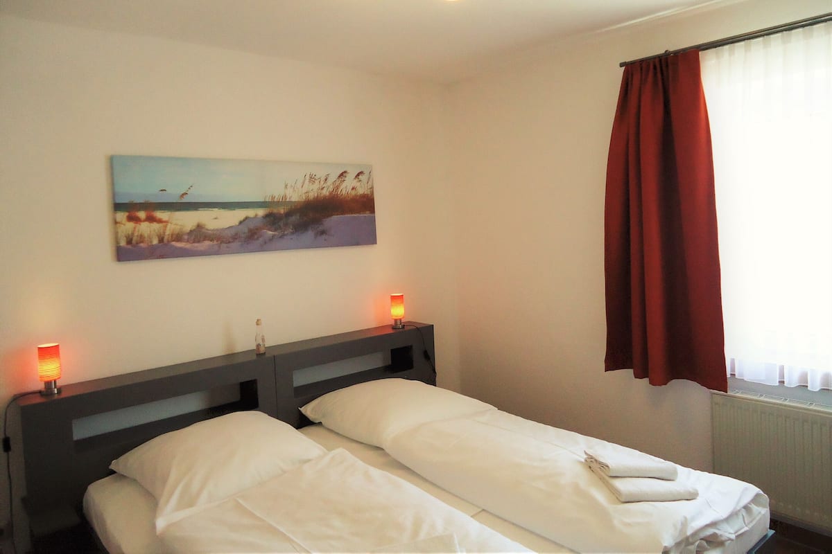 A hotel room with a bed, a painting on the wall, and a window with curtains.