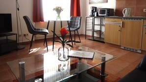 A modern living room with a glass coffee table, two chairs, a TV, and a dining area with a small table and chairs. - Uns Wiek-Hus (Mönchgut-Granitz)