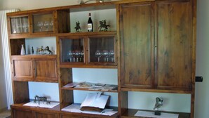 Un mueble de madera con varios estantes, algunos con cristalería y figuritas, y un jarrón con flores en el estante inferior.