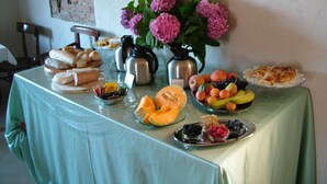 Una mesa de buffet con diversos alimentos, como pan, frutas y pasteles, además de estaciones de café y té.