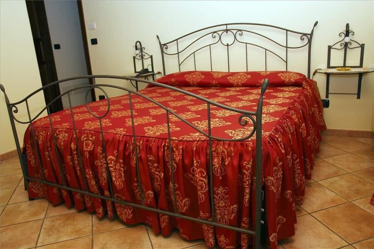 Een bed met een metalen frame en een rode sprei met een gouden patroon.