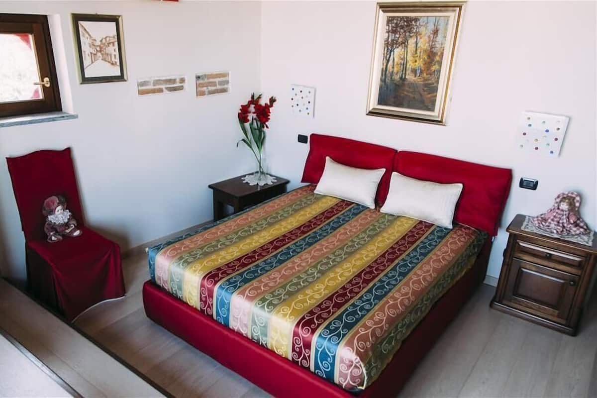 Een slaapkamer met een groot bed, een rode stoel, een nachtkastje en een schilderij aan de muur.