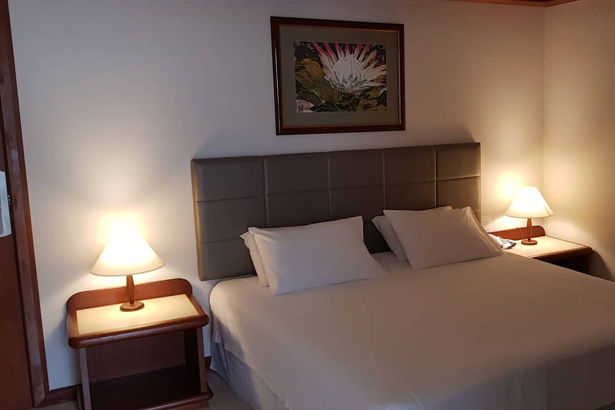 Una cama bien hecha con cabecera, dos mesitas de noche con lámparas y un cuadro en la pared.