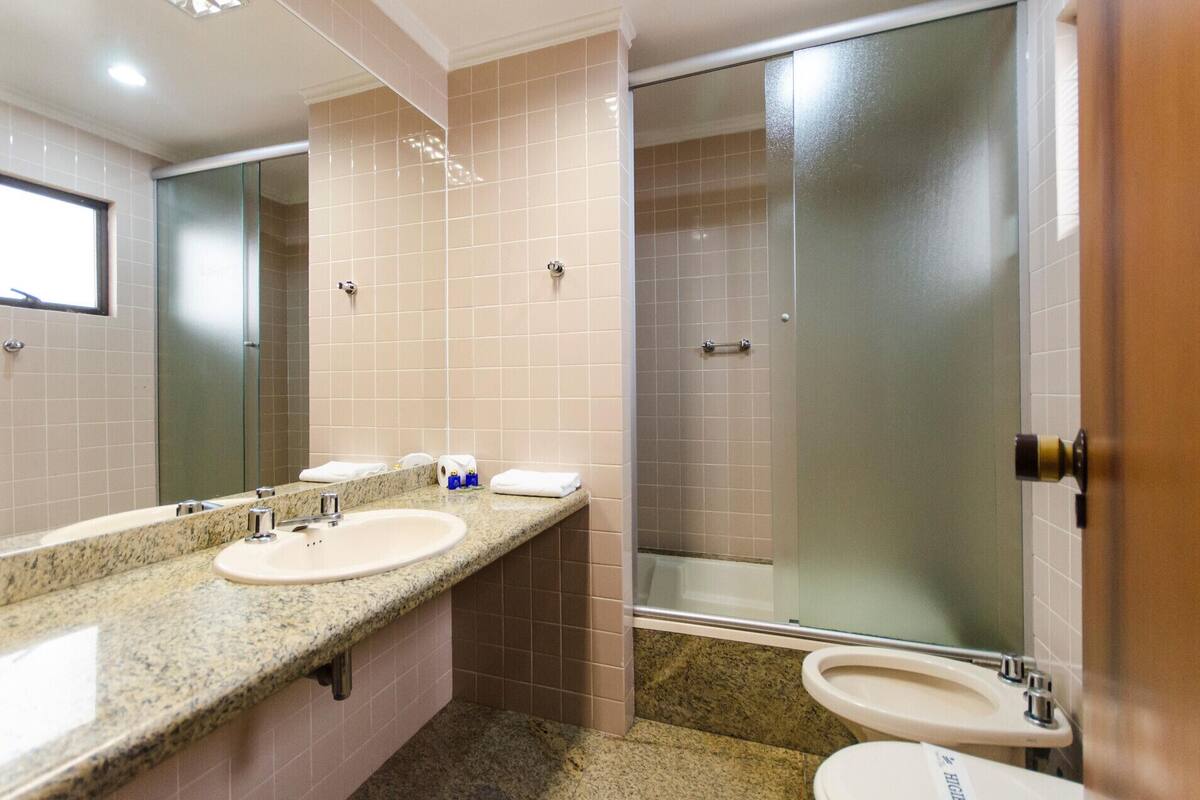 Un baño con dos lavamanos, ducha y puerta de vidrio.